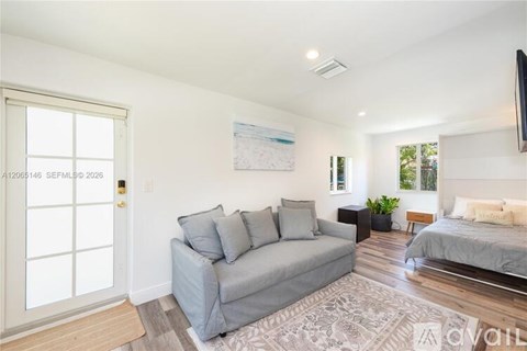A living room with a grey couch and a bed in the background.