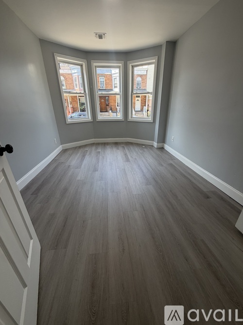 A room with grey walls and wooden flooring with a white door on the left.