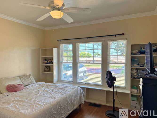 A bedroom with a bed, a fan, and a window with blinds.