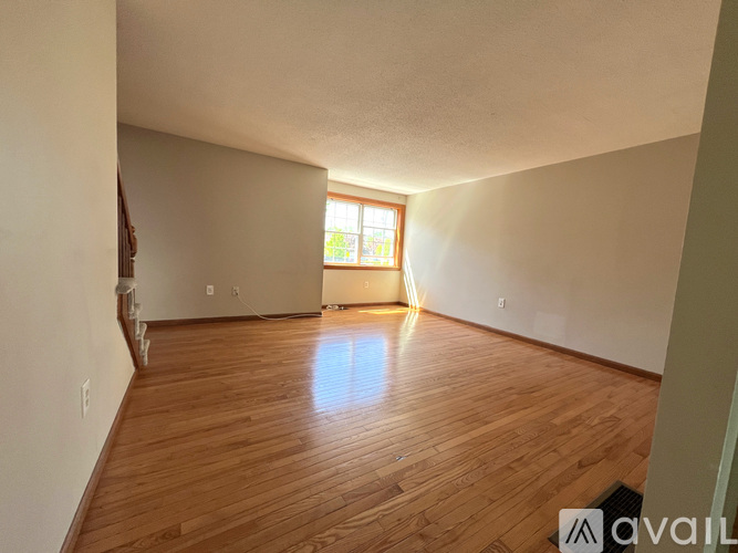 A room with wooden flooring and a window letting in sunlight.