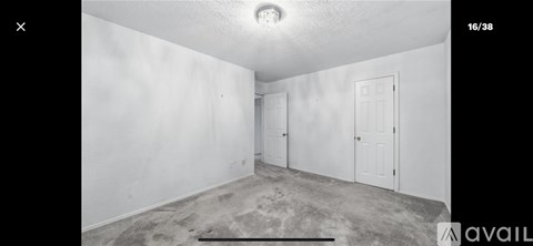 A room with white walls and a carpeted floor with a door on the right.