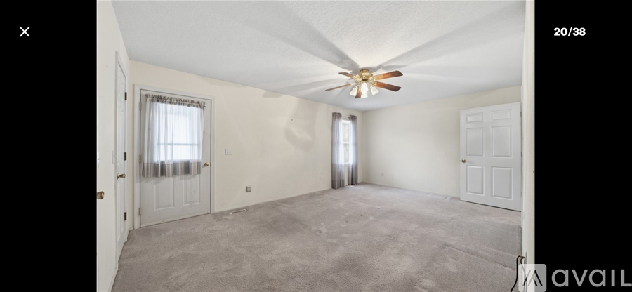 A spacious room with a ceiling fan and two windows.