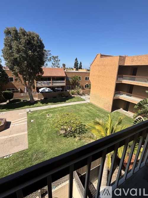A balcony overlooks a courtyard with a tree, bushes, and a building.