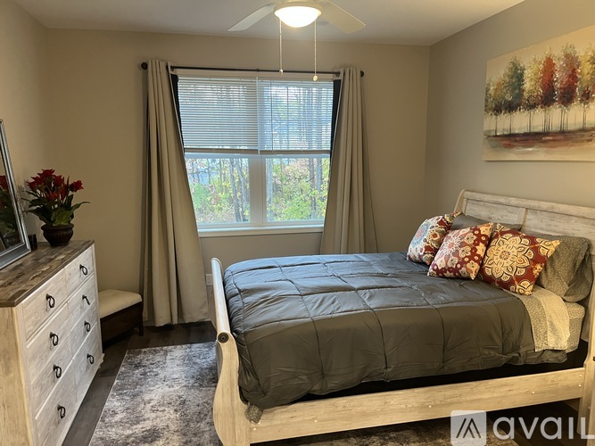 A bedroom with a bed, dresser, and window with curtains.
