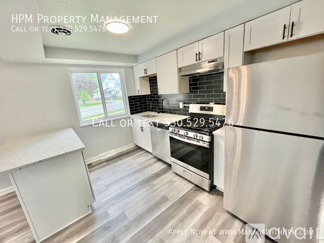 A modern kitchen with a stainless steel refrigerator, a stove, and a dining area with a window.
