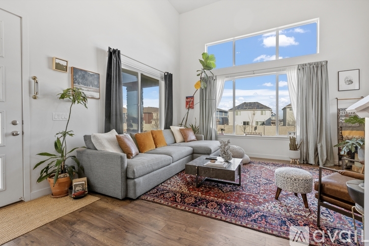 A living room with a grey couch, a coffee table, and a large window with curtains.