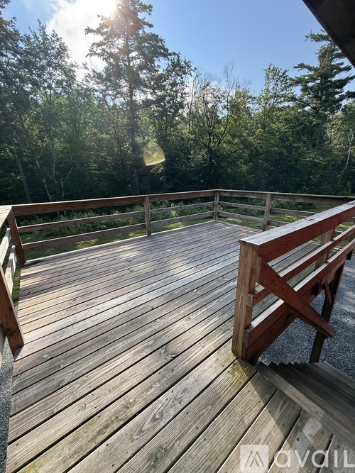 A wooden deck with a bench and trees in the background.