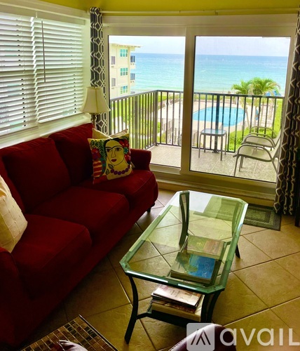 A red couch with a glass table in front of a balcony overlooking the ocean.