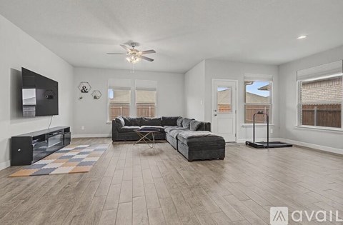 A spacious living room with a grey sofa set and a flat screen TV mounted on the wall.