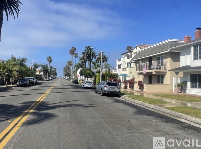A street with cars parked on the side and palm trees lining the road.