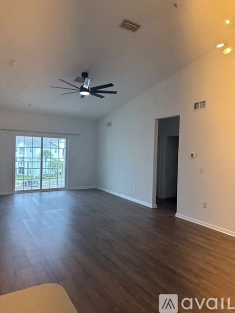 A spacious room with a ceiling fan and sliding glass doors leading to a balcony.
