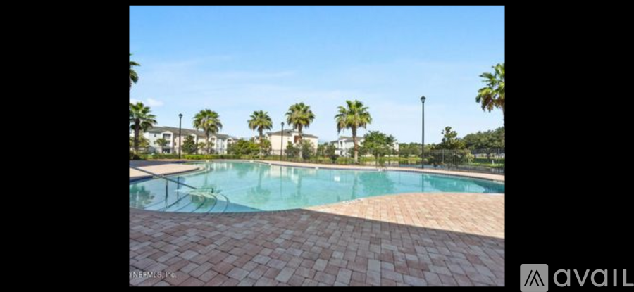 A pool surrounded by palm trees and a brick walkway.