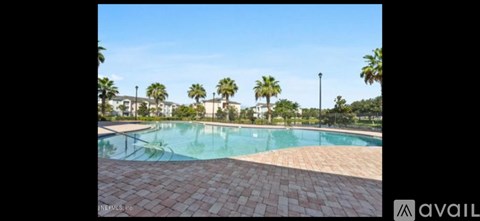 A pool surrounded by palm trees and a brick walkway.