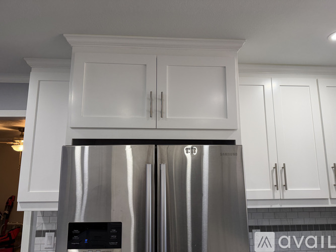 A stainless steel refrigerator with a digital display and white cabinets above it.