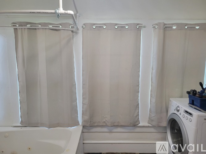 A bathroom with a tub, shower curtains, and a washing machine.