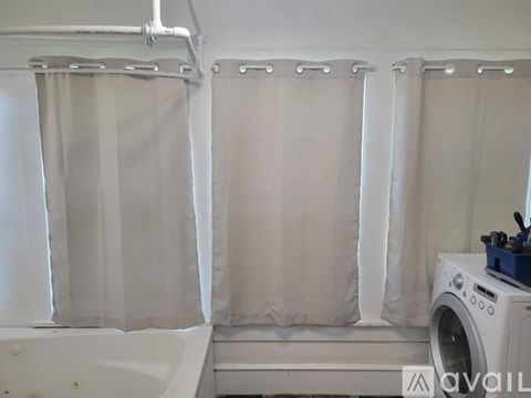 A bathroom with a tub, shower curtains, and a washing machine.