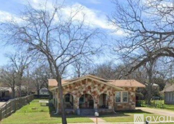 A house with a stone facade is surrounded by a fence and trees.