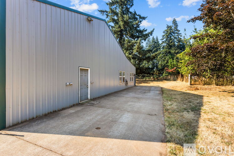 A large metal building with a green door and windows is surrounded by trees.