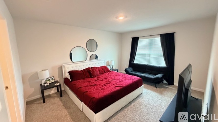 A bedroom with a red bedspread and a black chair.