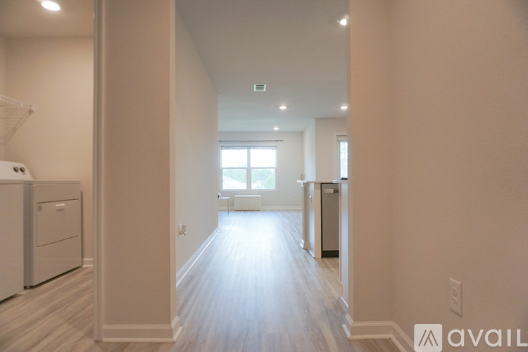 A spacious kitchen with white cabinets and a refrigerator, leading to a bright room with a window.