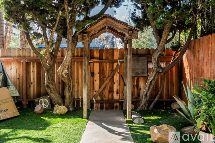 A wooden gazebo is surrounded by trees and rocks in a backyard.
