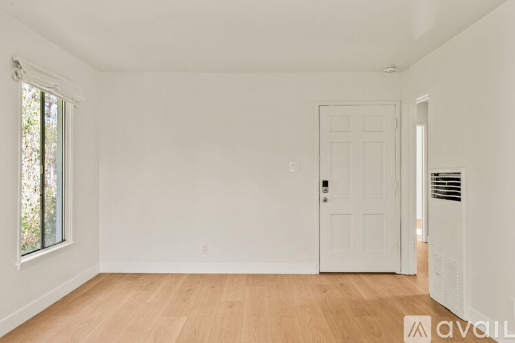 A room with a white door and a window with a view of trees.