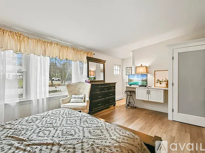 A bedroom with a bed, chair, and a dresser with a mirror above it.