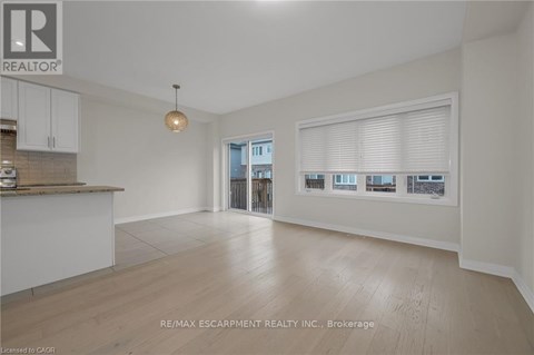 A spacious room with wooden flooring and a large window with blinds.