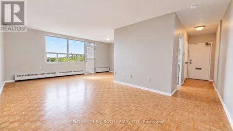 A spacious room with wooden flooring and white walls, featuring a large window and a door.