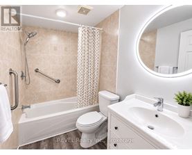 A bathroom with a white toilet, a bathtub with a shower head, a sink, and a round mirror.