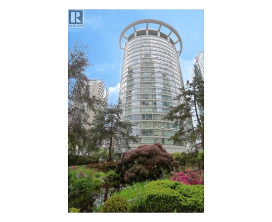 A tall building with a circular top is surrounded by greenery.