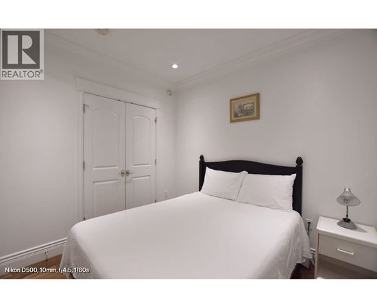 A bedroom with a white bed and a small nightstand with a lamp.