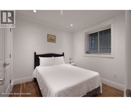 A bedroom with a bed, nightstand, and window.