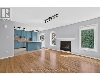A large, empty living room with a fireplace and a kitchen area in the background.