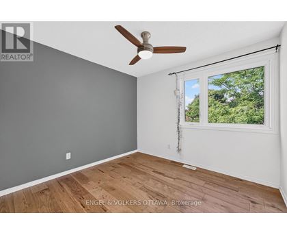 A room with a ceiling fan and a window showing trees outside.