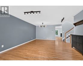 A spacious room with wooden floors and a staircase on the right side.