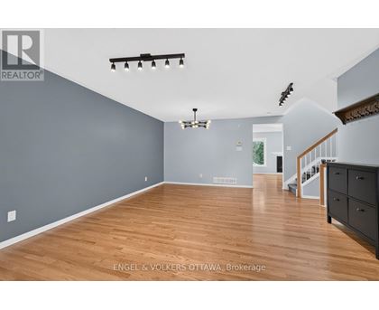 A spacious room with wooden floors and a staircase on the right side.