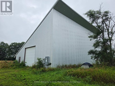 A large white building with a green roof is surrounded by grass and trees.