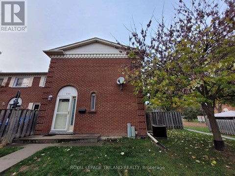 A small brick house with a white door and a tree in front.