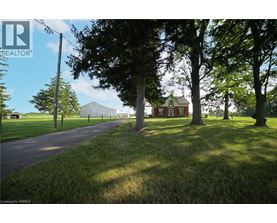 A house is situated in a grassy area with trees and a road leading to it.