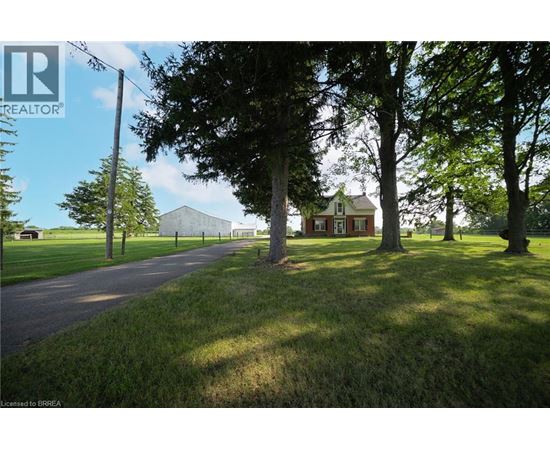 A house is situated in a grassy area with trees and a road leading to it.