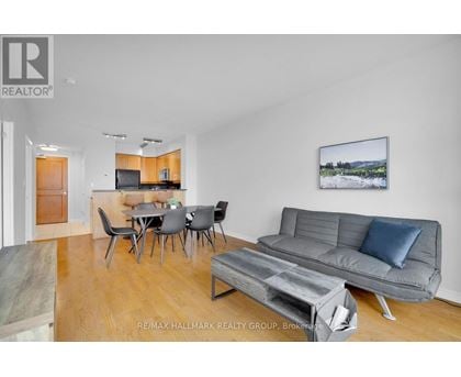 A living room with a grey couch, a dining table with chairs, and a painting on the wall.