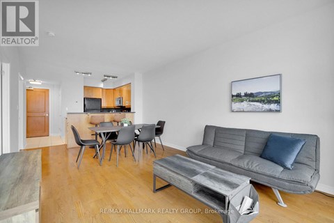 A living room with a grey couch, a dining table with chairs, and a painting on the wall.