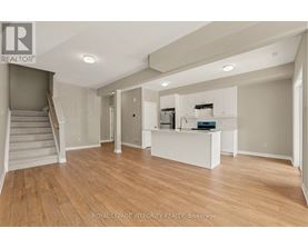 A spacious room with wooden flooring and a staircase on the left side.