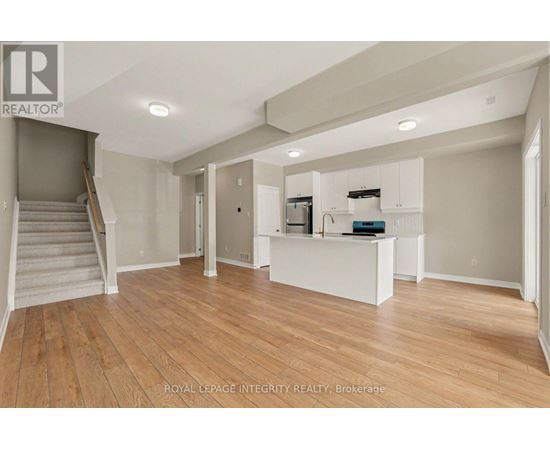 A spacious room with wooden flooring and a staircase on the left side.