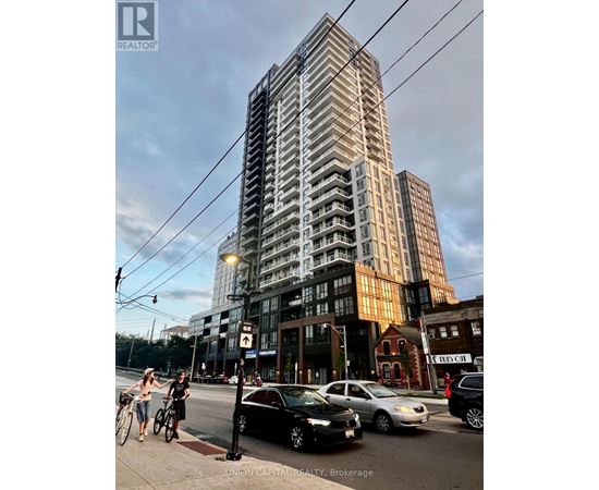 A tall building with a glass facade is the focal point of the image, with people walking and cars parked in front.