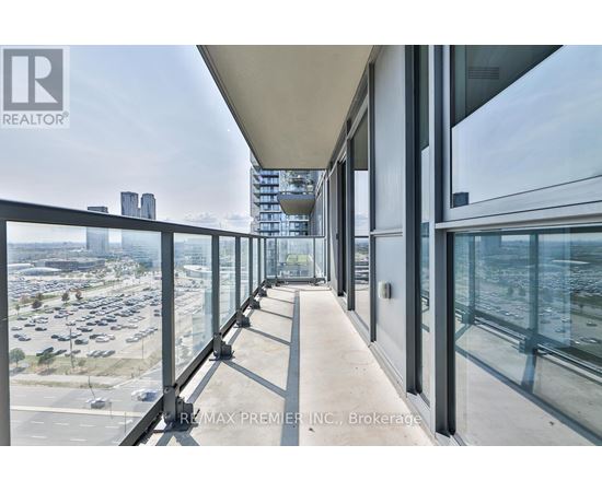 A balcony with glass railings overlooks a parking lot and buildings.