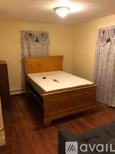 A bedroom with a bed, a grey ottoman, and a wooden floor.