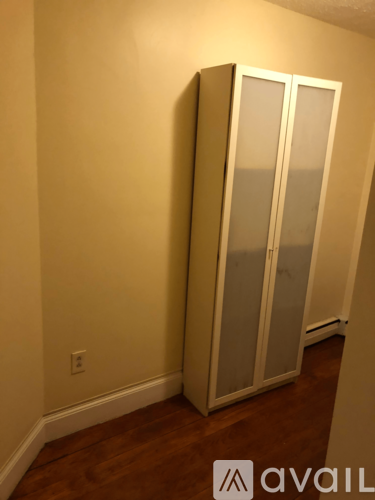 A tall white cabinet with glass doors stands in a room with a wooden floor.