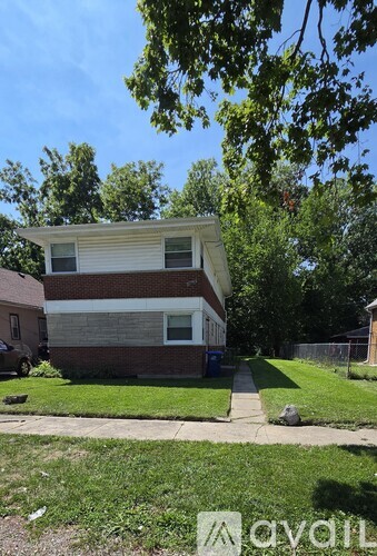 A two-story house with a brown and white exterior is surrounded by a green lawn and trees.